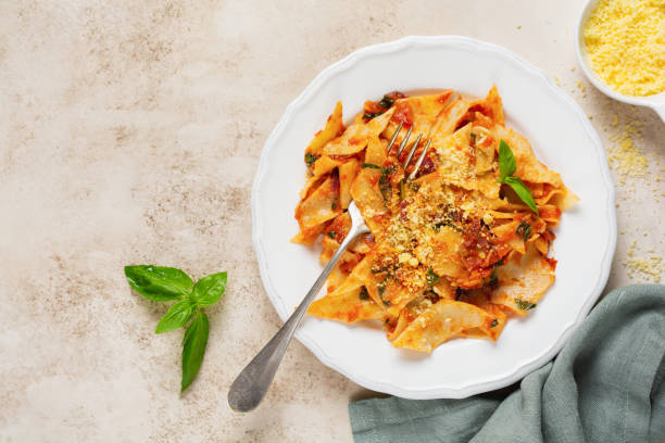istock Pasta Maltagliati with classic tomato sauce, parmesan and basil on a rustic concrete light table background. Traditional Italian dish serving. Top view. 1299804846