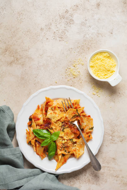 istock Pasta Maltagliati with classic tomato sauce, parmesan and basil on a rustic concrete light table background. Traditional Italian dish serving. Top view. 1299804876