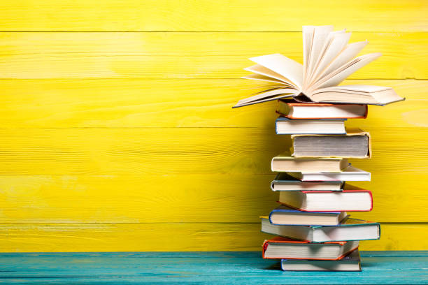 istock Books on bookshelf in Library. Back to School education concept on colored abstract yellow background. Open hardback book stack in a raw on wooden desk table. 1299805041