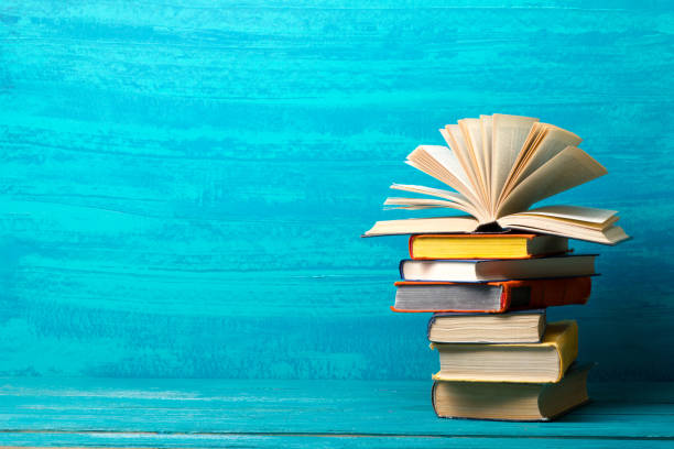 istock Books on bookshelf in Library. Back to School education concept on colored abstract blue background. Open hardback book stack in a raw on wooden desk table. 1299806447