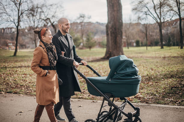 Young parents walking with baby carriage in park Man and woman, young mother and father walking in park with baby carriage. baby stroller winter stock pictures, royalty-free photos & images