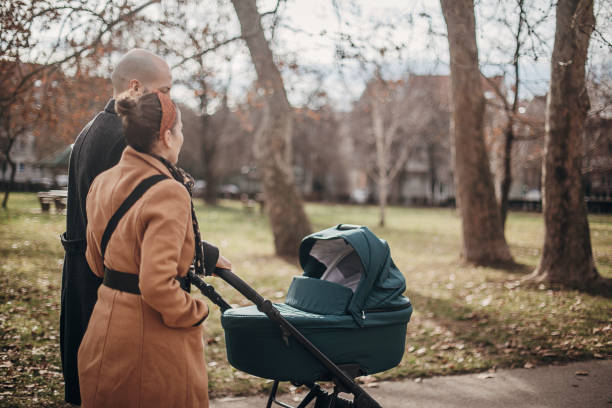 Young parents walking with baby carriage in park Man and woman, young mother and father walking in park with baby carriage. baby stroller winter stock pictures, royalty-free photos & images
