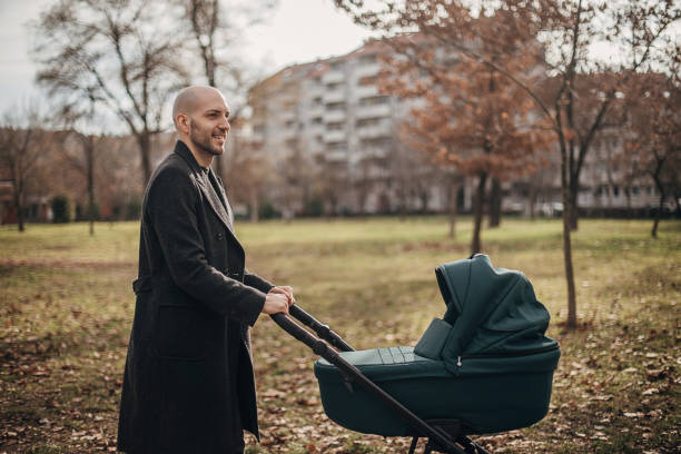 Young father taking a walk with baby carriage in park