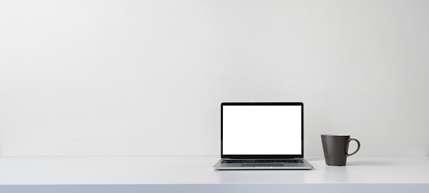 Modern contemporary workspace with blank screen laptop computer and coffee cup on office desk table on white wall background for copy space. Home office workplace concept.