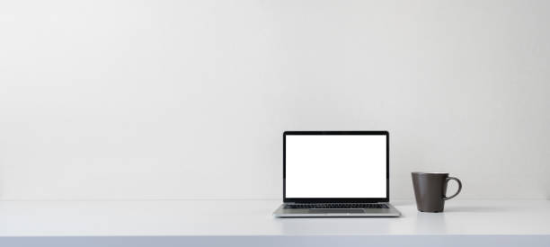 Modern contemporary workspace with blank screen laptop computer and coffee cup on office desk table on white background for copy space. Home office workplace concept. stock photo