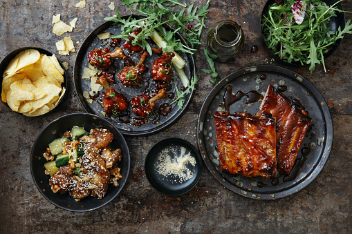 BBQ lollipop chicken wings with spicy BBQ glaze. Spicy glazed pork ribs. Tempura pork with vegetables. Flat lay top-down composition on dark background.