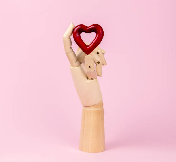 istock Human wooden hand model with heart on pastel pink. 1299809602