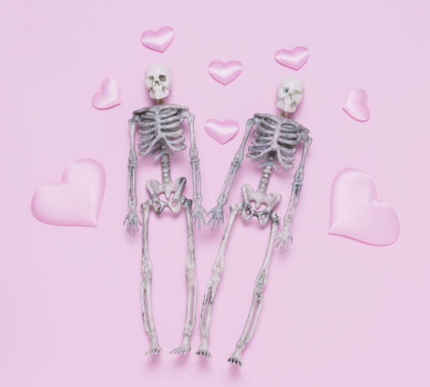 Top view skeleton couple and pink hearts pastel pink background.
