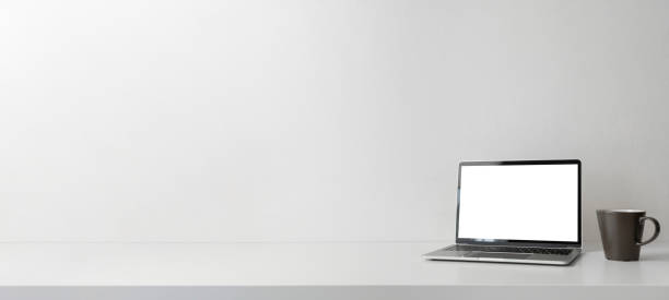 istock Modern contemporary workspace with blank screen laptop computer and coffee cup on office desk table on white background for copy space. Home office workplace concept. 1299810010