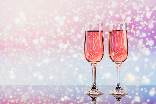 Two glasses of rose champagne with light snow bokeh as a background. Romantic dinner. Winter, Christmas or New Year holiday concept.
