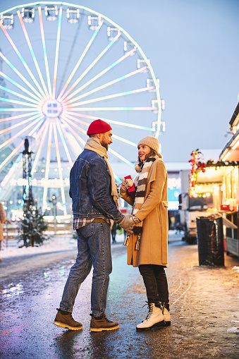 Cheerful caring man is giving present to beloved woman while walking in city centre at Christmas holidays