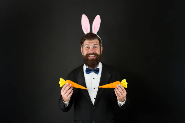 istock Businessman with long ears. Event host. Celebrate Easter. Bearded man with long ears. Play with carrots. Handsome elegant man wear bunny costume accessory. Celebration Easter holiday. Easter day 1299811098
