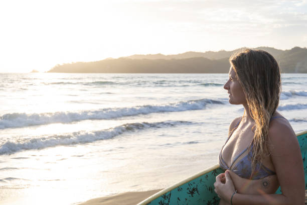 istock Young woman with boogie board relaxes on beach at sunrise 1299817738