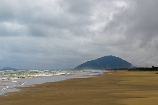 istock small waves in a calm sea, breaking on brown sand on an empty beach, with a distant mountain in the background under a cloudy sky. 1299818569