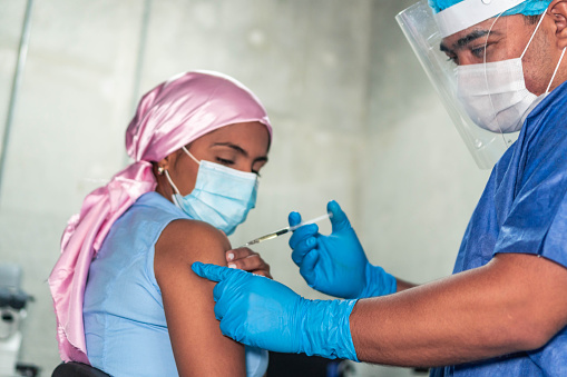 Nurse administering COVID-19 vaccine to a young woman with cancer.