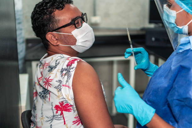 médecin administrant le vaccin pendant la pandémie - administering photos et images de collection