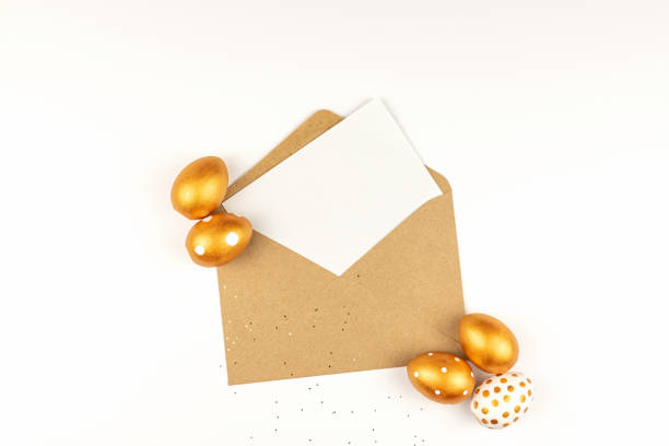 istock Easter festive decoration. Top view of easter eggs colored with golden paint and empty mock-up card in a kraft envelope. Various dotted designs. White background. 1299818758