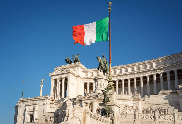 Italian flag with King Victor Emmanuel II equestrian monument in background. Piazza Venezia, Rome, Italy. stock photo