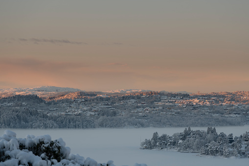 Early morning in winter in a fjord (Nordasvannet) near the City of Bergen on the west coast of Norway at sunrise after snowfall. The seawater of the fjord is frozen and covered with snow.