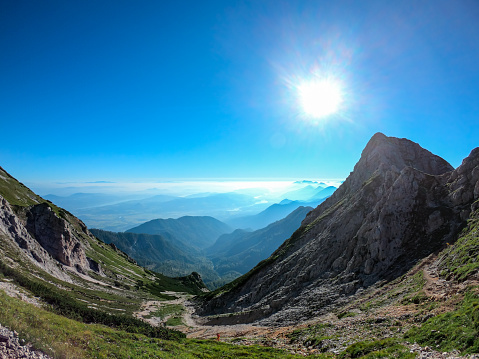 A panoramic view on the Alps from the top of Mittagskogel in Austrian Alps. Clear and sunny day. U-shaped valley. A bit of haze in the valley. Outdoor activity. Alpine mountain chains in the back