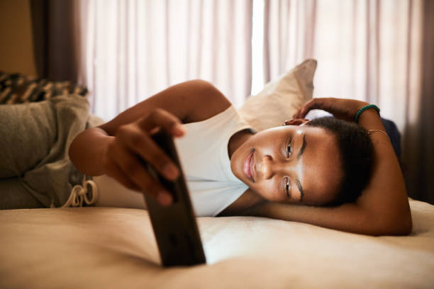 istock Smiling young woman lying on her bed watching something on her phone 1299823651