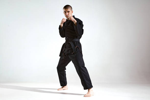 istock Sportive guy trainer in black kimono fighter posing in karate stance on studio background with copy space 1299827705