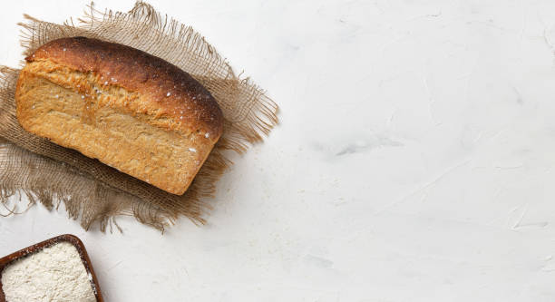 A loaf of white rustic bread on a linen lining on a white table. Small business idea, baking healthy natural sourdough bread to order. Top view with copy space