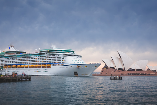 Royal Caribbean cruise ship Voyager of the Seas approaches Sydney Opera House and Sydney Harbour on a summer morning at sunrise.