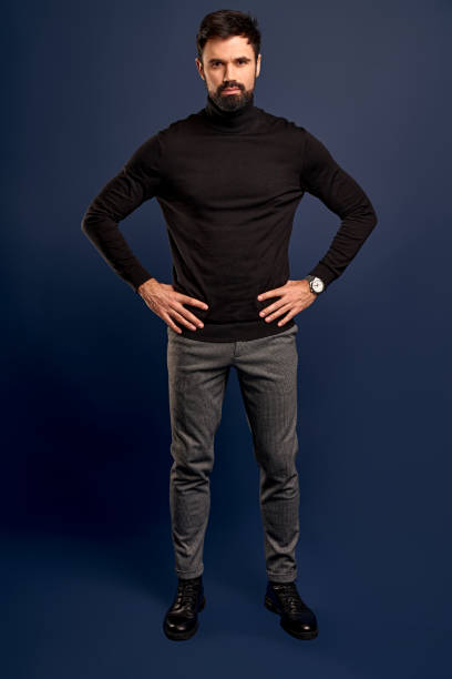 istock Full length of charming young man looking at camera and holds his hands aside while standing against Pacific Blue background 1299830621