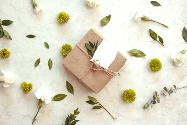 istock Spring holiday  floral background - white background with brown paper wrapped gift, green chrysanthemum, white carnations and eucalyptus leaves. 1299830697