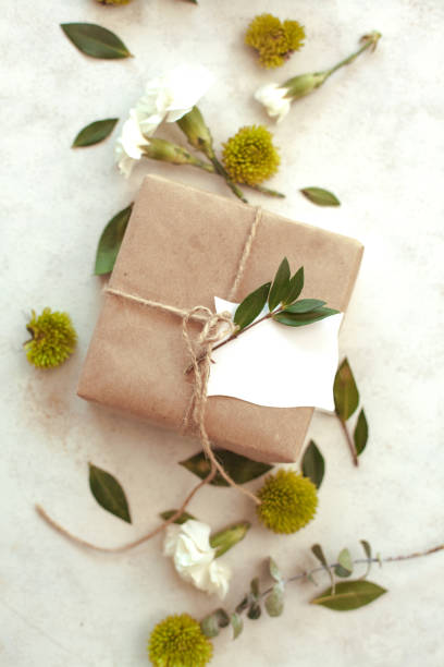 istock Spring holiday  floral background - white background with brown paper wrapped gift, green chrysanthemum, white carnations and eucalyptus leaves. 1299831050