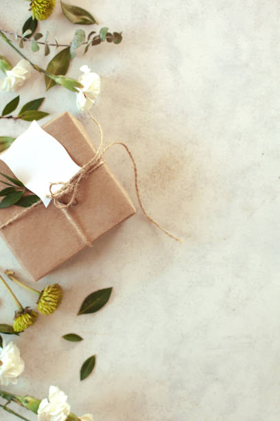 istock Spring holiday  floral background - white background with brown paper wrapped gift, green chrysanthemum, white carnations and eucalyptus leaves with copy space. 1299831901