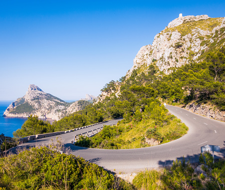 An empty hairpin bend on a road on Majorca's Cap de Formentor, with the mediterranean sea visible on the horizon.