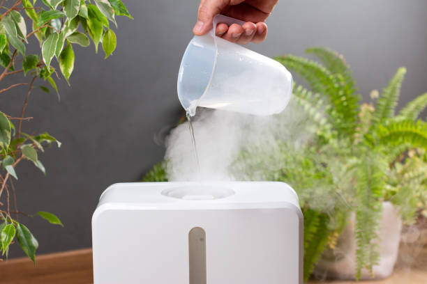 un hombre usa un humidificador en casa. llenar el depósito con agua - humidifier steam home interior appliance fotografías e imágenes de stock