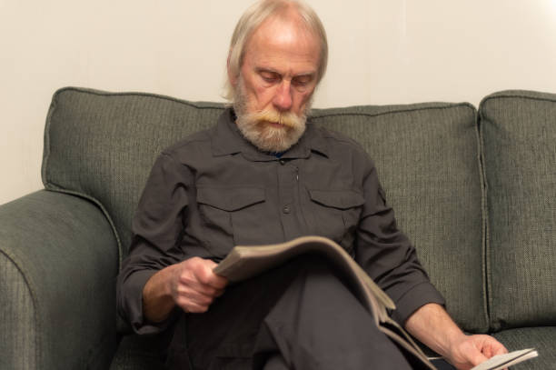 istock Senior man sitting on a sofa in his home reading a newspaper 1299835610