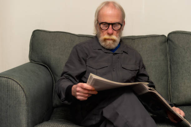 istock Retired man sitting on a sofa in his home reading a newspaper 1299835903