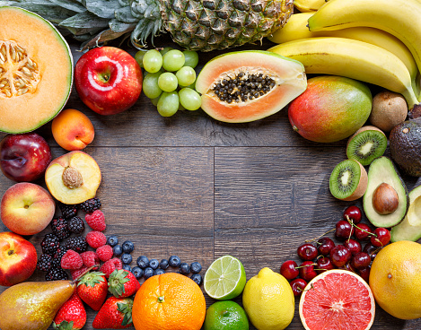 A variety of fresh fruits arranged on a wooden background with copy space in the center.