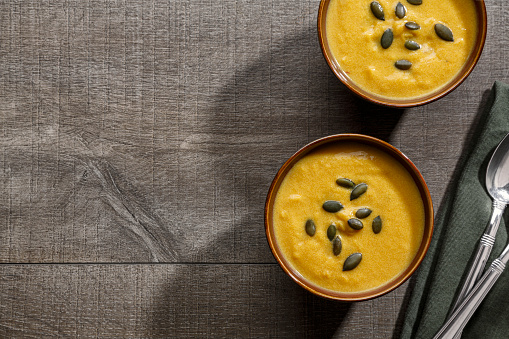 A vegetarian butternut squash soup made primarily from butternut squash and other root vegetables in bowls on a neutral wood background.