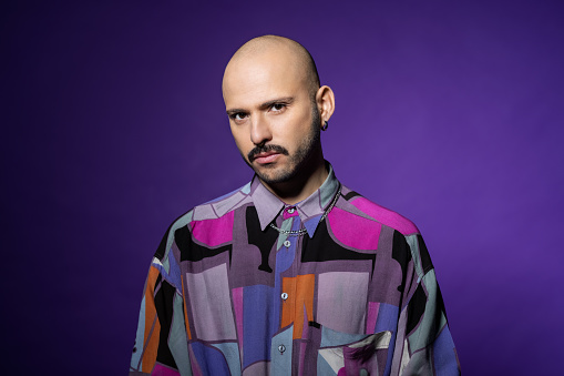 Serious looking man on purple background. Man with shaved head staring at camera.