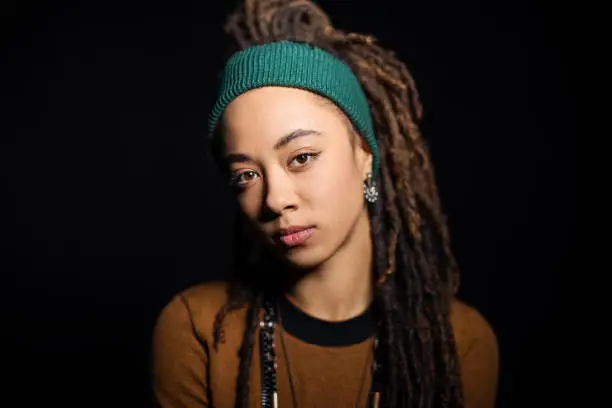 Portrait of confident young woman wearing casuals on black background. African American female with locs hairstyle looking at camera.