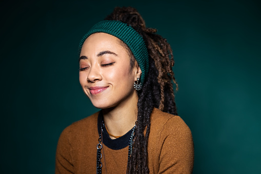 Portrait of a beautiful african american woman with her eyes closed. Young woman in casuals wearing headband and having locs hairstyle against green background.