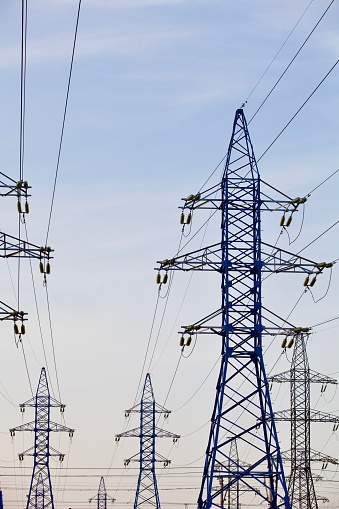 High voltage power lines pylons and electrical cables on a clear blue sky background. Modern infrastructure of high voltage transmission lines. Overhead power lines towers equipment. Energy industry. long-distance supply of electricity via high-voltage transmission lines.