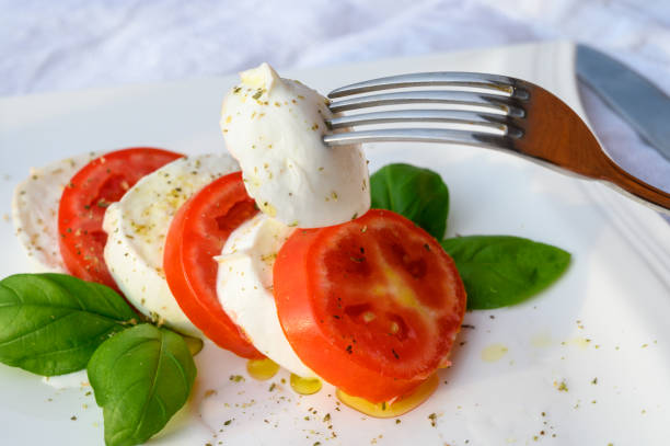 insalata caprese a base di mozzarella fresca di formaggio bianco morbido, basilico verde, pomodori rossi ed erbe origano - caprese salad foto e immagini stock