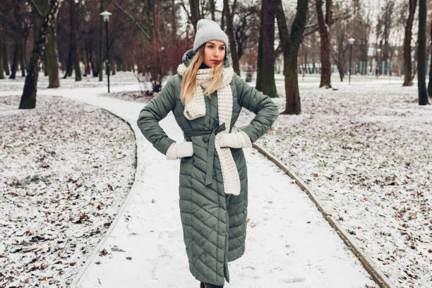 冬の女性ファッション。雪の公園でスカーフ、帽子、ミトンと長い緑のコートを着た若い女性。 - scarf hat green glove ストックフォトと画像