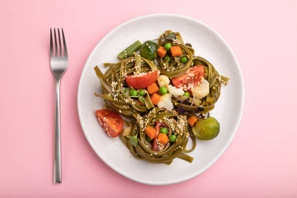 istock Tagliatelle green spinach pasta with tomato, pea and microgreen sprouts on a pastel pink background. Top view, flat lay, close up. 1299847229