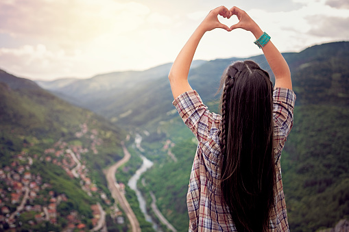 Young woman is doing heart with her hands on the mountain peek