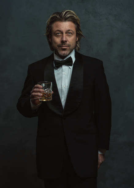 Satisfied blonde man with stubble beard in tuxedo holding glass of whisky. Satisfied blonde man with stubble beard in tuxedo holding glass of whisky. black men with blonde hair stock pictures, royalty-free photos & images