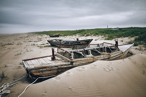Fishing old wooden boats on the beach sand near the sea, green grass and cloudy sky. Sakhalin island, Russia