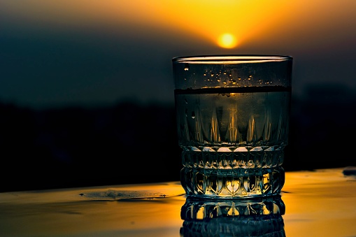 A glass kept on a wet surface and sun setting down in background. Reflection of glass on surface