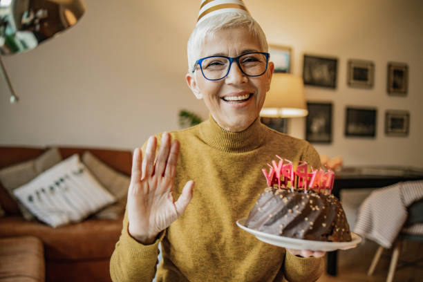 Portrait of senior woman holding birthday cake A mature woman is holding a birthday cake and looking at the camera virtual birthday celebration stock pictures, royalty-free photos & images